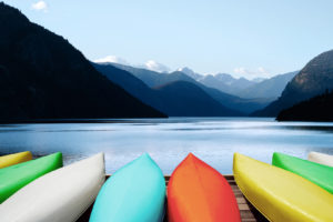 Eight canoes lined up on a wooden dock waiting to launch into the smooth clear waters of a calm lake that is surrounded by tall rocky mountains.