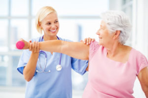 Therapist Assisting Senior Patient In Lifting Dumbbell